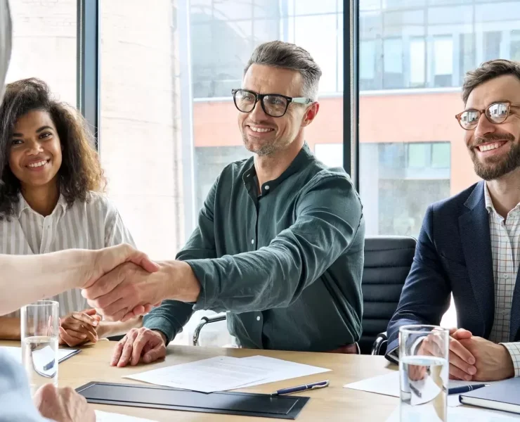 Business meeting with handshake and smiling participants.